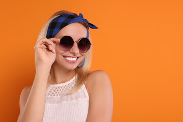 Sticker - Portrait of smiling hippie woman in sunglasses on orange background. Space for text