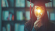 © Keitma - College student girl showing a light bulb for education, E-learning graduate certificate and business concept, woman with graduation regalia hat for creative thinking idea and human development