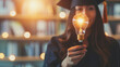 College student girl showing a light bulb for education, E-learning graduate certificate and business concept, woman with graduation regalia hat for creative thinking idea and human development