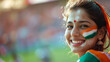 Happy Indian woman supporter with face painted in India flag colors, green white and orange, female fan at a sports event such as cricket or field hockey match, blurry stadium background, copy space