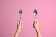 Woman hands showing spoon and fork isolated on pink color pastel background