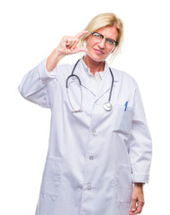 Sticker - Middle age blonde doctor woman over isolated background smiling and confident gesturing with hand doing size sign with fingers while looking and the camera. Measure concept.