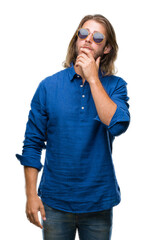 Sticker - Young handsome man with long hair wearing sunglasses over isolated background with hand on chin thinking about question, pensive expression. Smiling with thoughtful face. Doubt concept.