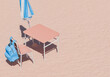 © Antonio Solano - top view of a blue backpack on a school chair next to a desk under a blue striped beach umbrella on sandy texture, summer study concept.