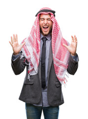 Poster - Young handsome arabian man with long hair wearing keffiyeh over isolated background celebrating mad and crazy for success with arms raised and closed eyes screaming excited. Winner concept