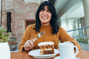 portrait of young very happy latin woman sitting eating carrot cake in u restaurant