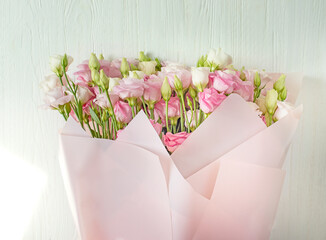 Wall Mural - A bouquet of delicate pink and white eustoma lisianthus flowers in pink paper on a white wooden background