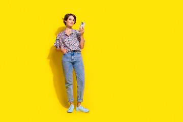 Wall Mural - Full body portrait of lovely lady use smart phone empty space ad blank isolated on yellow color background