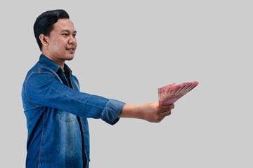 Young Asian man showing happy face expression while giving paper money and looking empty space