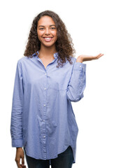 Wall Mural - Young hispanic business woman smiling cheerful presenting and pointing with palm of hand looking at the camera.