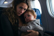 Tired young mother and baby sitting together in airplane cabin near window. Travel, vacation, difficult flight with children