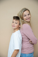 Wall Mural - cool young teenager boy with white t-shirt posing together with his beautiful mother in front of brown background