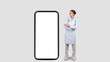© Prostock-studio - Happy caucasian millennial doctor in white coat point finger at big phone with empty screen