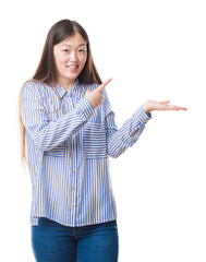 Sticker - Young Chinese woman over isolated background amazed and smiling to the camera while presenting with hand and pointing with finger.