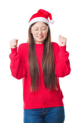 Wall Mural - Young Chinese woman over isolated background wearing christmas hat excited for success with arms raised celebrating victory smiling. Winner concept.