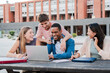 © Jose Calsina - Group of young classmates studying together and preparing a exam using a laptop, browsing on internet at university campus. Teenage students smiling and doing the homeworks with a notepad computer