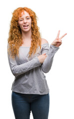 Wall Mural - Young redhead woman smiling with happy face winking at the camera doing victory sign. Number two.