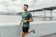 Man in sportswear jogging along a city waterfront promenade, with a serene water view.