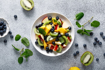 Wall Mural - Fruit and berry salad with mango, kiwi, apple, blueberry and fresh mint leaves. Healthy food, diet. Top view