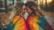 Lesbian couple snuggling and covering with rainbow flag 