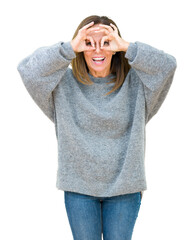 Poster - Beautiful middle age woman wearing winter sweater over isolated background doing ok gesture like binoculars sticking tongue out, eyes looking through fingers. Crazy expression.