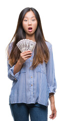 Wall Mural - Young asian woman holding dollars over isolated background scared in shock with a surprise face, afraid and excited with fear expression