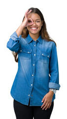 Wall Mural - Young beautiful brunette woman wearing blue denim shirt over isolated background doing ok gesture with hand smiling, eye looking through fingers with happy face.