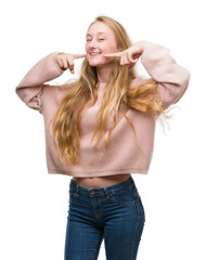 Wall Mural - Blonde teenager woman wearing pink sweater smiling confident showing and pointing with fingers teeth and mouth. Health concept.