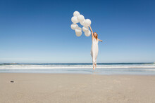 Young Woman Holding Bunch Of White Balloons, Smiling And Laughing In The Camera On The Beach. Cape Town, South Africa