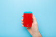 Young adult man hand holding and showing red plastic stick of armpit deodorant on light blue table background. Pastel color. Male daily beauty product. Closeup. Top down view.