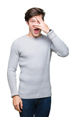 Wall Mural - Young handsome man wearing winter sweater over isolated background peeking in shock covering face and eyes with hand, looking through fingers with embarrassed expression.