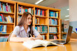 © atsarapong - Young female student studying at a table in the university library, working on a laptop computer.