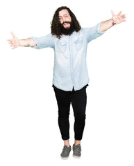 Wall Mural - Young hipster man with long hair and beard wearing glasses looking at the camera smiling with open arms for hug. Cheerful expression embracing happiness.