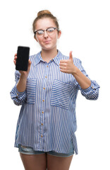 Wall Mural - Young blonde woman using smartphone happy with big smile doing ok sign, thumb up with fingers, excellent sign