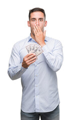 Canvas Print - Handsome young man holding money cover mouth with hand shocked with shame for mistake, expression of fear, scared in silence, secret concept