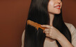 © Dasha Petrenko - Young happy brunette woman combing her long healthy brown hair and smiling at camera while posing isolated on dark background