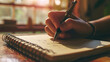 Close-up of a person's hand writing in a notebook with a pen, with a warm and cozy ambiance