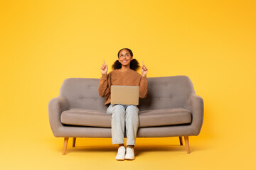 Wall Mural - black student girl pointing fingers up sitting with laptop, studio