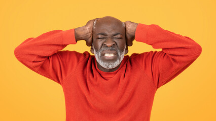 Wall Mural - Frustrated senior man in a red sweater and hat, clutching his head with a grimace