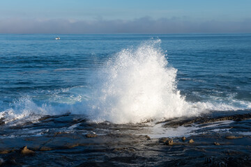 Wall Mural - 2020-01-03 WATER CRASHING ON THE ROCKY SHORELINE CAUSING SPRAY WITH A CALM PACIFIC OCEAN IN THE BACKGROUND AND A BOAT IN THE BACKGROUND IN LA JOLLA CALIFORNIA