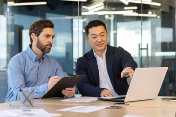 In an office setting, two businessmen review content on a laptop, investing time in a focused business meeting and strategy planning.