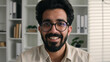 © Yuliia - Webcam view happy Arabian indian muslim man in glasses male teacher tutor businessman talk to computer web camera smiling video chat online educational course talking job interview from home office