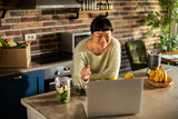 Fototapeta Tulipany - Happy woman making smoothie while watching online recipe on laptop in kitchen