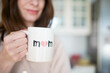 © silvia - Caucasian woman, smiling happy about being a mother, holding a mother's day cup with 'mom' written on it. Pink, airy background.