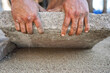 Installing new pavement or floor outside from large concrete tiles, closeup detail on male worker fitting stone block over sand and gravel base layer