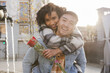 © Aida - boyfriend piggybacks his girlfriend while she hugs him and carries a bouquet of red roses valentine's day gift on their anniversary walking through the city at sunset