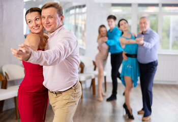 Positive people of different ages dancing tango in pairs in dance hall