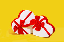 Two White Heart-shaped Gift Boxes With Red Ribbons On A Yellow Background