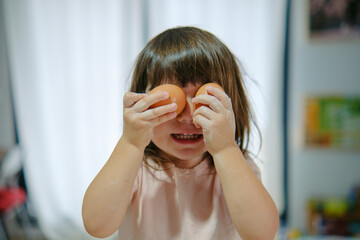 Niña pequeña sonriendo colocando dos huevos en los ojos 