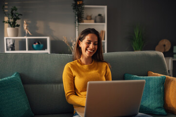 Beautiful woman working on laptop and smiling while sitting on the couch at home